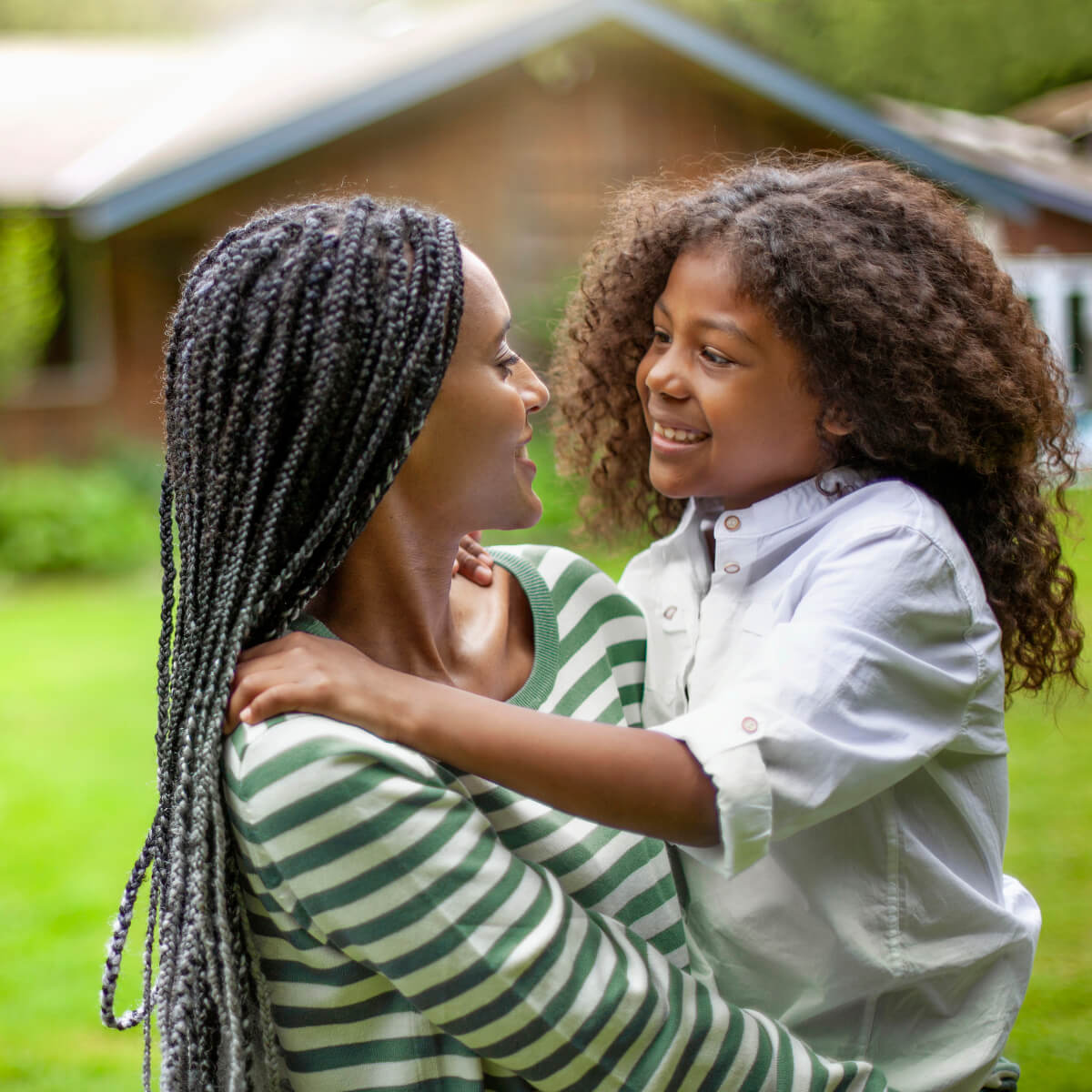 Une mère coiffée de longues tresses tient son enfant devant leur maison. Droit au logement